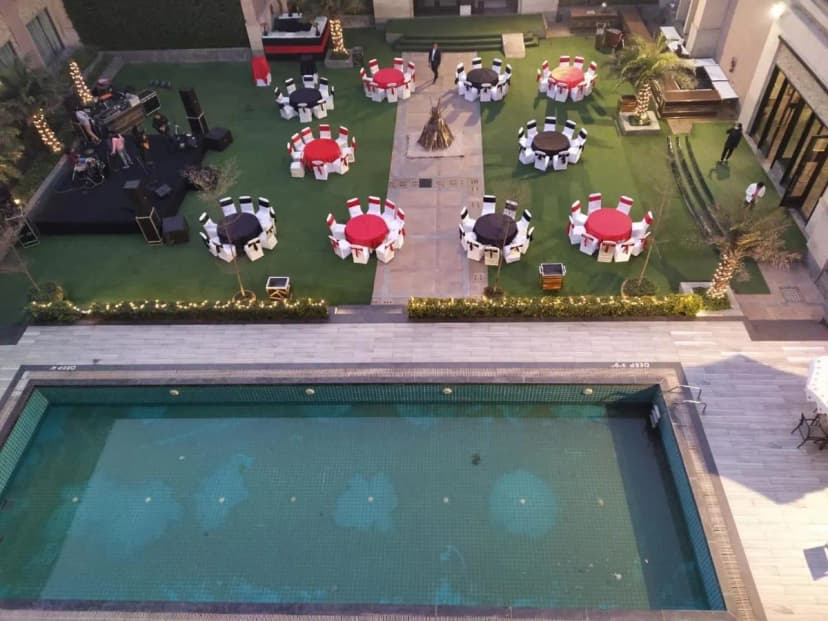 An elegant outdoor wedding venue with poolside seating, round tables dressed in red, white, and black, and a live band setup for entertainment
