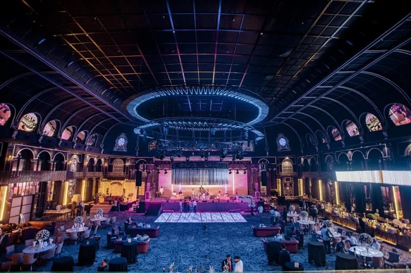 A luxurious, grand indoor wedding venue with elegant decor, dramatic lighting, a central dance floor, and opulent seating arrangements perfect for upscale celebrations